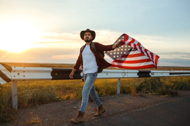 4 Temmuz. 4 Temmuz. Ulusal bayrağı olan Amerikalı. Amerikan bayrağı. Bağımsızlık günü. Vatanseverlik tatili. Adam şapka, sırt çantası, gömlek ve kot giyiyor. Güzel günbatımı ışık. 