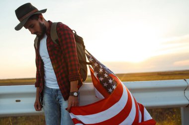 4 Temmuz. 4 Temmuz. Ulusal bayrağı olan Amerikalı. Amerikan bayrağı. Bağımsızlık günü. Vatanseverlik tatili. Adam şapka, sırt çantası, gömlek ve kot giyiyor. Güzel günbatımı ışık. 
