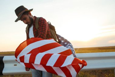 4 Temmuz. 4 Temmuz. Ulusal bayrağı olan Amerikalı. Amerikan bayrağı. Bağımsızlık günü. Vatanseverlik tatili. Adam şapka, sırt çantası, gömlek ve kot giyiyor. Güzel günbatımı ışık. 