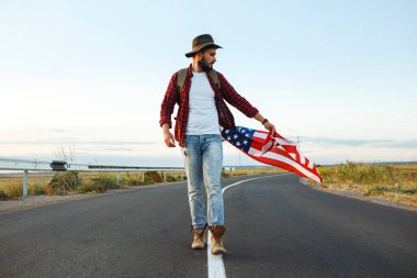 4 Temmuz. 4 Temmuz. Ulusal bayrağı olan Amerikalı. Amerikan bayrağı. Bağımsızlık günü. Vatanseverlik tatili. Adam şapka, sırt çantası, gömlek ve kot giyiyor. Güzel günbatımı ışık. 