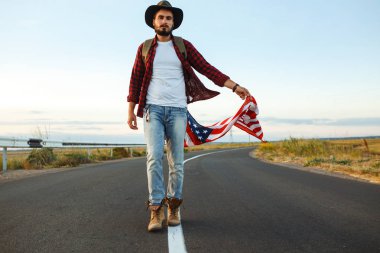 4 Temmuz. 4 Temmuz. Ulusal bayrağı olan Amerikalı. Amerikan bayrağı. Bağımsızlık günü. Vatanseverlik tatili. Adam şapka, sırt çantası, gömlek ve kot giyiyor. Güzel günbatımı ışık. 