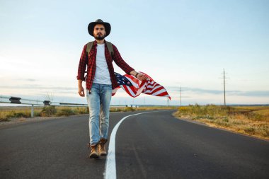 4 Temmuz. 4 Temmuz. Ulusal bayrağı olan Amerikalı. Amerikan bayrağı. Bağımsızlık günü. Vatanseverlik tatili. Adam şapka, sırt çantası, gömlek ve kot giyiyor. Güzel günbatımı ışık. 