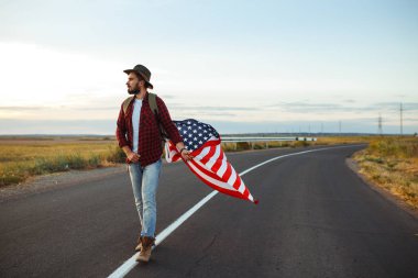 4 Temmuz. 4 Temmuz. Ulusal bayrağı olan Amerikalı. Amerikan bayrağı. Bağımsızlık günü. Vatanseverlik tatili. Adam şapka, sırt çantası, gömlek ve kot giyiyor. Güzel günbatımı ışık. 