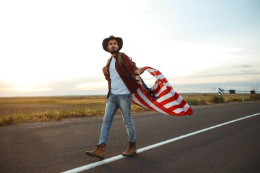 4 Temmuz. 4 Temmuz. Ulusal bayrağı olan Amerikalı. Amerikan bayrağı. Bağımsızlık günü. Vatanseverlik tatili. Adam şapka, sırt çantası, gömlek ve kot giyiyor. Güzel günbatımı ışık. 