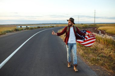 4 Temmuz. 4 Temmuz. Ulusal bayrağı olan Amerikalı. Amerikan bayrağı. Bağımsızlık günü. Vatanseverlik tatili. Adam şapka, sırt çantası, gömlek ve kot giyiyor. Güzel günbatımı ışık. 