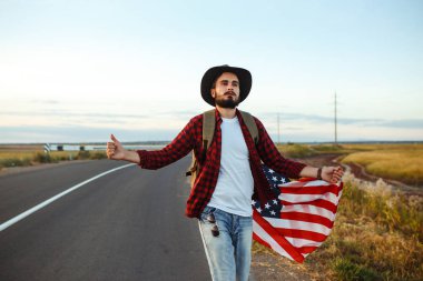 4 Temmuz. 4 Temmuz. Ulusal bayrağı olan Amerikalı. Amerikan bayrağı. Bağımsızlık günü. Vatanseverlik tatili. Adam şapka, sırt çantası, gömlek ve kot giyiyor. Güzel günbatımı ışık. 