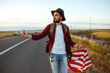 4 Temmuz. 4 Temmuz. Ulusal bayrağı olan Amerikalı. Amerikan bayrağı. Bağımsızlık günü. Vatanseverlik tatili. Adam şapka, sırt çantası, gömlek ve kot giyiyor. Güzel günbatımı ışık. 