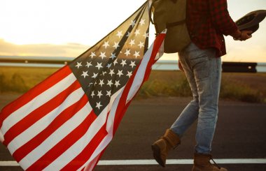 4 Temmuz. 4 Temmuz. Ulusal bayrağı olan Amerikalı. Amerikan bayrağı. Bağımsızlık günü. Vatanseverlik tatili. Adam şapka, sırt çantası, gömlek ve kot giyiyor. Güzel günbatımı ışık. 