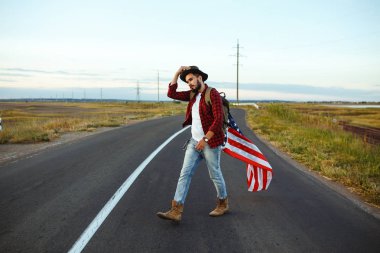 4 Temmuz. 4 Temmuz. Ulusal bayrağı olan Amerikalı. Amerikan bayrağı. Bağımsızlık günü. Vatanseverlik tatili. Adam şapka, sırt çantası, gömlek ve kot giyiyor. Güzel günbatımı ışık. 