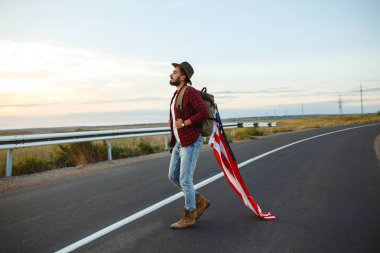 4 Temmuz. 4 Temmuz. Ulusal bayrağı olan Amerikalı. Amerikan bayrağı. Bağımsızlık günü. Vatanseverlik tatili. Adam şapka, sırt çantası, gömlek ve kot giyiyor. Güzel günbatımı ışık. 