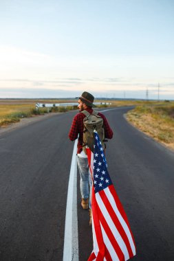 4 Temmuz. 4 Temmuz. Ulusal bayrağı olan Amerikalı. Amerikan bayrağı. Bağımsızlık günü. Vatanseverlik tatili. Adam şapka, sırt çantası, gömlek ve kot giyiyor. Güzel günbatımı ışık. 