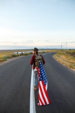 4 Temmuz. 4 Temmuz. Ulusal bayrağı olan Amerikalı. Amerikan bayrağı. Bağımsızlık günü. Vatanseverlik tatili. Adam şapka, sırt çantası, gömlek ve kot giyiyor. Güzel günbatımı ışık. 