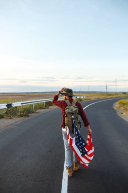 4 Temmuz. 4 Temmuz. Ulusal bayrağı olan Amerikalı. Amerikan bayrağı. Bağımsızlık günü. Vatanseverlik tatili. Adam şapka, sırt çantası, gömlek ve kot giyiyor. Güzel günbatımı ışık. 