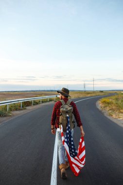 4 Temmuz. 4 Temmuz. Ulusal bayrağı olan Amerikalı. Amerikan bayrağı. Bağımsızlık günü. Vatanseverlik tatili. Adam şapka, sırt çantası, gömlek ve kot giyiyor. Güzel günbatımı ışık. 