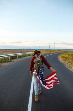 4 Temmuz. 4 Temmuz. Ulusal bayrağı olan Amerikalı. Amerikan bayrağı. Bağımsızlık günü. Vatanseverlik tatili. Adam şapka, sırt çantası, gömlek ve kot giyiyor. Güzel günbatımı ışık. 