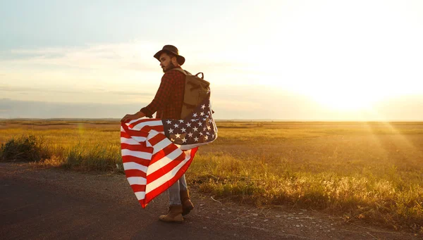 4 Temmuz. 4 Temmuz. Ulusal bayrağı olan Amerikalı. Amerikan bayrağı. Bağımsızlık günü. Vatanseverlik tatili. Adam şapka, sırt çantası, gömlek ve kot giyiyor. Güzel günbatımı ışık. 