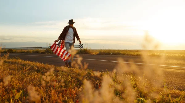 4 Temmuz. 4 Temmuz. Ulusal bayrağı olan Amerikalı. Amerikan bayrağı. Bağımsızlık günü. Vatanseverlik tatili. Adam şapka, sırt çantası, gömlek ve kot giyiyor. Güzel günbatımı ışık. 