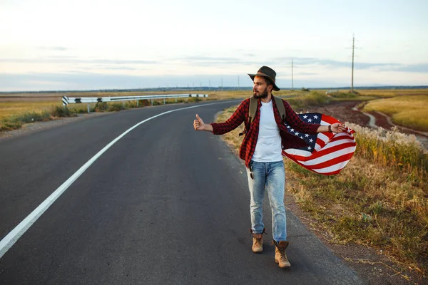 4 Temmuz. 4 Temmuz. Ulusal bayrağı olan Amerikalı. Amerikan bayrağı. Bağımsızlık günü. Vatanseverlik tatili. Adam şapka, sırt çantası, gömlek ve kot giyiyor. Güzel günbatımı ışık. 