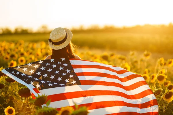 ヒマワリ畑にアメリカ国旗を持つ美少女 7月4日7月4日自由 夕焼けの光 女の子は微笑む美しい夕日 独立記念日 愛国的な休日 — ストック写真
