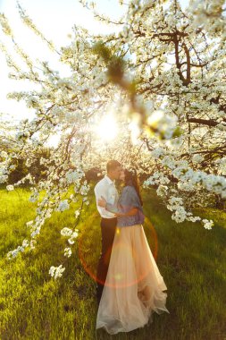 Güzel bir gelinin portresi. Düğün konsepti. Şık bir düğün. Harika gün batımı ışığı. Mavi kot ceket giyiyor, elbise. Bahar çiçekli bahçe..