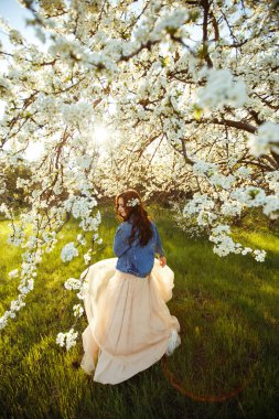 Güzel bir gelinin portresi. Düğün konsepti. Şık bir düğün. Harika gün batımı ışığı. Mavi kot ceket giyiyor, elbise. Bahar çiçekli bahçe..
