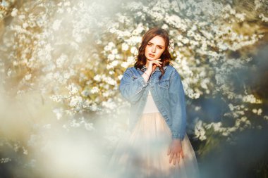 Güzel bir gelinin portresi. Düğün konsepti. Şık bir düğün. Harika gün batımı ışığı. Mavi kot ceket giyiyor, elbise. Bahar çiçekli bahçe..