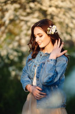 Güzel bir gelinin portresi. Düğün konsepti. Şık bir düğün. Harika gün batımı ışığı. Mavi kot ceket giyiyor, elbise. Bahar çiçekli bahçe..