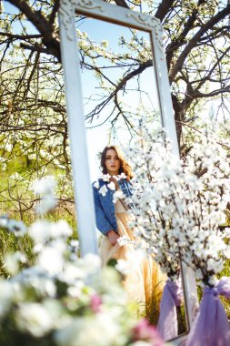 Güzel bir gelinin portresi. Düğün konsepti. Şık bir düğün. Harika gün batımı ışığı. Mavi kot ceket giyiyor, elbise. Bahar çiçekli bahçe..