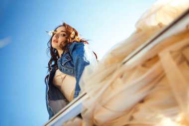 Güzel bir gelinin portresi. Düğün konsepti. Şık bir düğün. Harika gün batımı ışığı. Mavi kot ceket giyiyor, elbise. Bahar çiçekli bahçe..