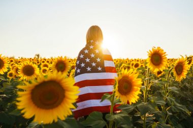 Ayçiçeği tarlasında Amerikan bayrağı olan güzel bir kız. 4 Temmuz. 4 Temmuz. Özgürlük. Gün batımı ışığı Kız gülümsüyor. Güzel gün batımı. Bağımsızlık Günü. Vatansever tatil. 