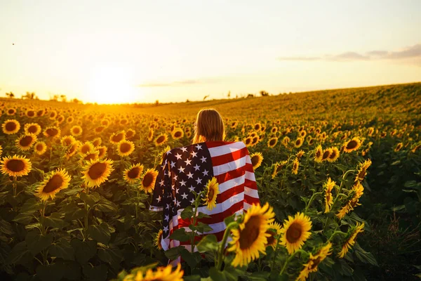 美丽的女孩 在向日葵的田野里插着美国国旗 7月4日7月4日自由 夕阳灯 女孩微笑 美丽的日落 独立日爱国假期 — 图库照片