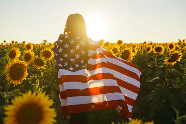 美丽的女孩 在向日葵的田野里插着美国国旗 7月4日7月4日自由 夕阳灯 女孩微笑 美丽的日落 独立日爱国假期 — 图库照片