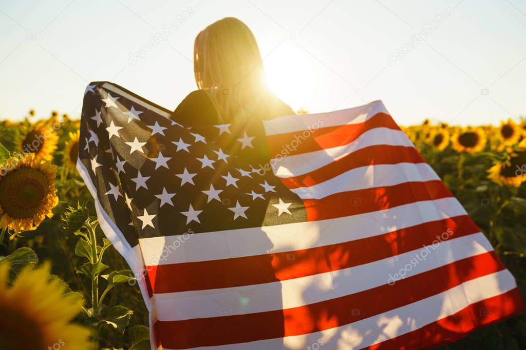 Beautiful girl with the American flag in a sunflower field. 4th of July. Fourth of July. Freedom. Sunset light The girl smiles. Beautiful sunset. Independence Day. Patriotic holiday. 