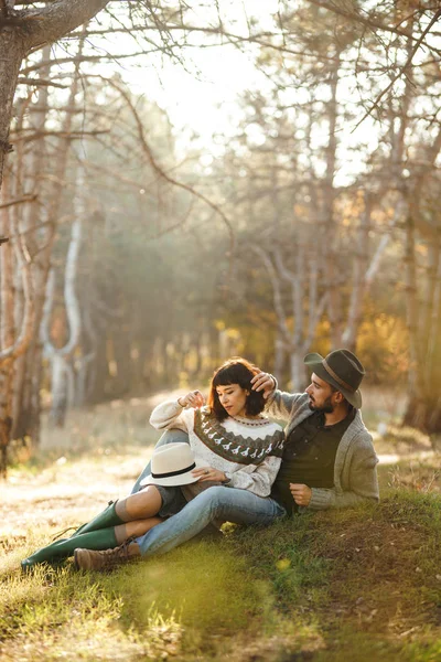 Lovely hipster couple looking at each other. Couple wearing beautiful hats and sweaters. Lifestyle, happy couple of two play on a sunny day in the park. The concept of youth, love and lifestyle. Sunset in autumn