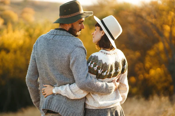 Lovely hipster couple looking at each other. Couple wearing beautiful hats and sweaters. Lifestyle, happy couple of two play on a sunny day in the park. The concept of youth, love and lifestyle. Sunset in autumn