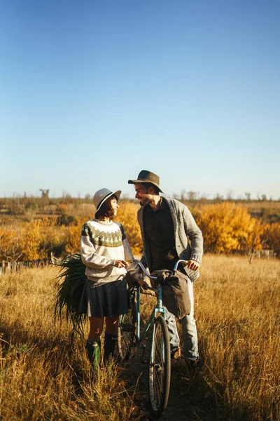 Lovely hipster couple with bike. Couple wearing beautiful hats and sweaters. Lifestyle, happy couple of two play on a sunny day in the park. The concept of youth, love and lifestyle. Sunset in autumn