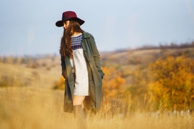 Paltolu güzel, genç, şık bir kız sonbaharda parkta yürüyor. Kız yeşil bir ceket ve kırmızı bir şapka giyiyor. Güzel bir akşam. Sonbahar modası. Yaşam tarzı. Yüksek moda portresi.