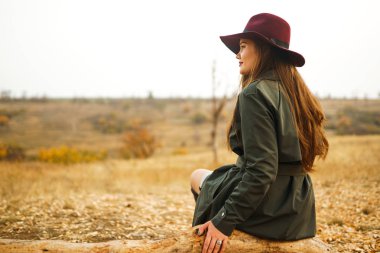 Paltolu güzel, genç, şık bir kız sonbaharda parkta yürüyor. Kız yeşil bir ceket ve kırmızı bir şapka giyiyor. Güzel bir akşam. Sonbahar modası. Yaşam tarzı. Yüksek moda portresi.