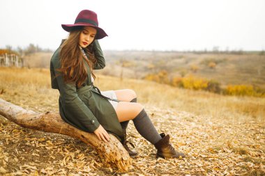 Paltolu güzel, genç, şık bir kız sonbaharda parkta yürüyor. Kız yeşil bir ceket ve kırmızı bir şapka giyiyor. Güzel bir akşam. Sonbahar modası. Yaşam tarzı. Yüksek moda portresi.