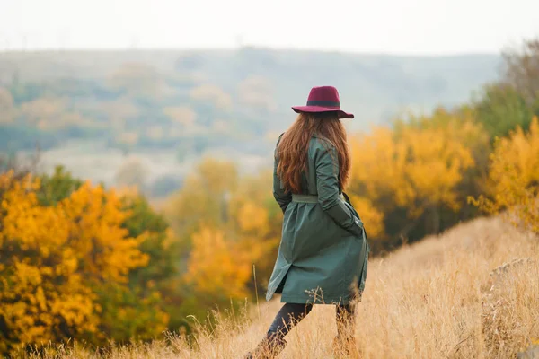 コートを着た美しい若いスタイリッシュな女の子が公園の秋に歩きます 少女は緑のコートと赤い帽子で服を着ている 美しい夜だ秋のファッション ライフスタイルファッション性の高い肖像 — ストック写真