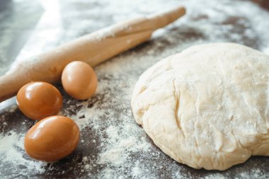 Hamur, merdane, yumurta ve un ahşap masada. Mutfak masasındaki malzemelerle birlikte çiğ pizza hamuru. Koyu arkaplan. 