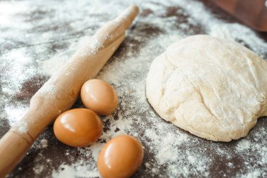 Hamur, merdane, yumurta ve un ahşap masada. Mutfak masasındaki malzemelerle birlikte çiğ pizza hamuru. Koyu arkaplan. 