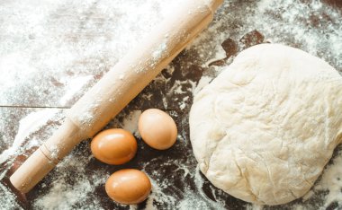 Hamur, merdane, yumurta ve un ahşap masada. Mutfak masasındaki malzemelerle birlikte çiğ pizza hamuru. Koyu arkaplan. 