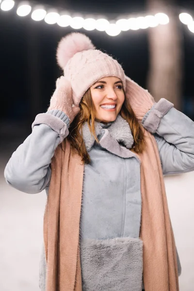 Beautiful young woman in the winter time. Happy winter time in the forest.The girl is dressed in a blue coat, in a light knitted hat, scarf and mittens. Festive garland lights. Christmas, new year.