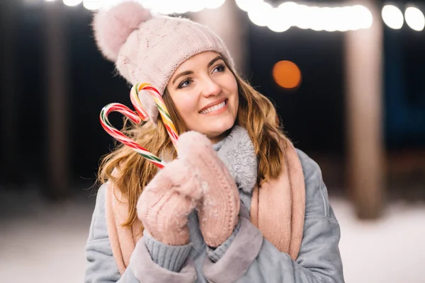 美しい女の子は甘いキャラメル缶を手に持っています 森の中の幸せな冬の時間 女の子は薄手のニット帽 スカーフ ミトンで青いコートを着ています お祭りのガーランドライト クリスマス — ストック写真