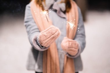 Maytap ellerinde. Ormanda mutlu kış zamanları. Kız mavi bir ceket giymiş, açık renk bir şapka, atkı ve eldiven takmış. Şenlikli çelenk ışıkları. Noel, yeni yıl.