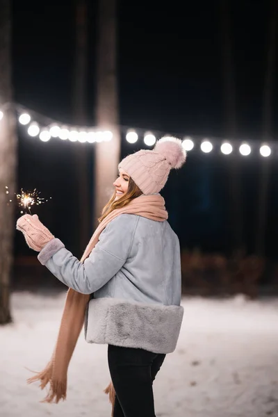 手に輝きを持つ美しい女の子 森の中で幸せな冬の時間 女の子は 薄手のニット帽 スカーフ ミトンで青いコートを着ています お祭りのガーランドライト クリスマス — ストック写真