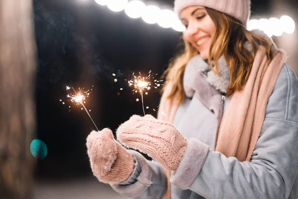 手にスパーカー 森の中で幸せな冬の時間 女の子は 薄手のニット帽 スカーフ ミトンで青いコートを着ています お祭りのガーランドライト クリスマス — ストック写真