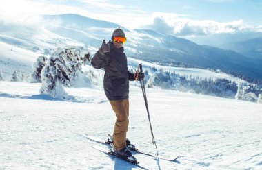 Dağlarda kayak yapan genç bir adam. Karlı dağlarda kayak yaparken, kış geliyor, kar yağıyor. Kışın aktif bir yaşam tarzı. Kayak merkezi sezonu açıldı. Kayak ekipmanları, patika. Olağanüstü kış sporları.