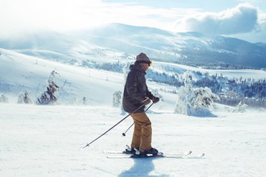 Dağlarda kayak yapan genç bir adam. Karlı dağlarda kayak yaparken, kış geliyor, kar yağıyor. Kışın aktif bir yaşam tarzı. Kayak merkezi sezonu açıldı. Kayak ekipmanları, patika. Olağanüstü kış sporları.